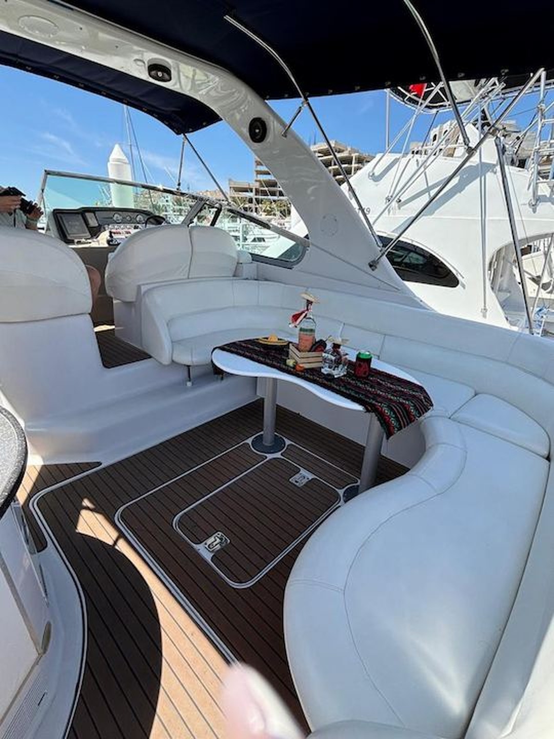 White wraparound yacht seating and a table beneath a dark canvas top at a marina
