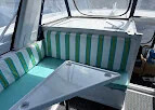 Green and white striped bench cushions around a table inside an enclosed yacht cockpit